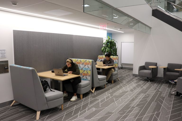 Two booths along a wall. A student sits in each both, both working on laptop computers.