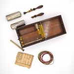 Open box next to 1890s battery and pieces