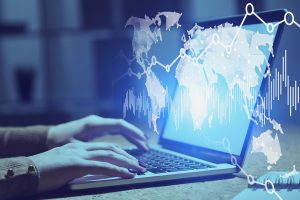 Woman hands typing on laptop in blurred office with double exposure of world map and graphs. 