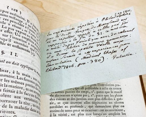 Closeup of a handwritten note stuck inside an open book. Text is in French.