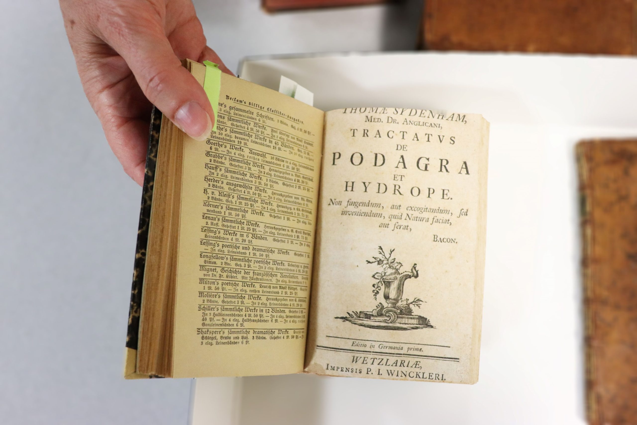 An old book is held open to the cover page of Tractatus de Podagra et Hydrope.