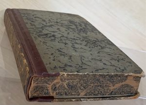 An antique book resting on a table. The cover and spine show some wear and tear.