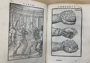 An book lying open on a table. The left page features an engraved image of men posed as if boxing in an arena with ancient Greek or Roman columns and statues. The page on the right is an illustration of three fists, each wrapped with strips of leather or fabric as boxing gloves. Image links to a larger version of the image.