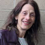 Headshot of a white woman with long brown hair, wearing a navy blazer and white shirt.