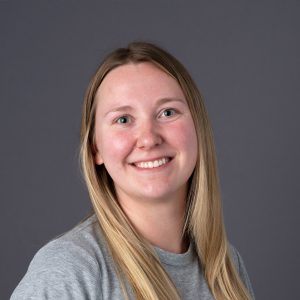 Headshot of a white woman with long blonde hair, wearing a gray shirt.